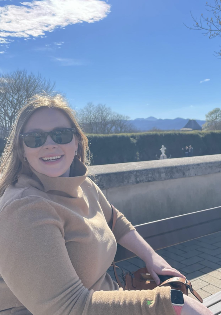 Picture of Melanie sitting on a bench outside with a mountain landscape in the background. 